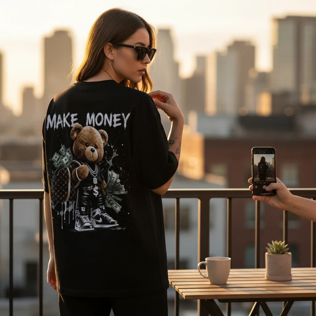 Woman wearing a black KLYRO FASHION oversized t-shirt with a graphic print of a teddy bear holding money on the back.