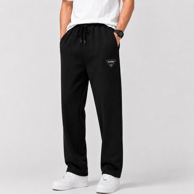 KLYRO FASHION men's black athletic track pants with a drawstring waist and logo patch, styled with white sneakers.