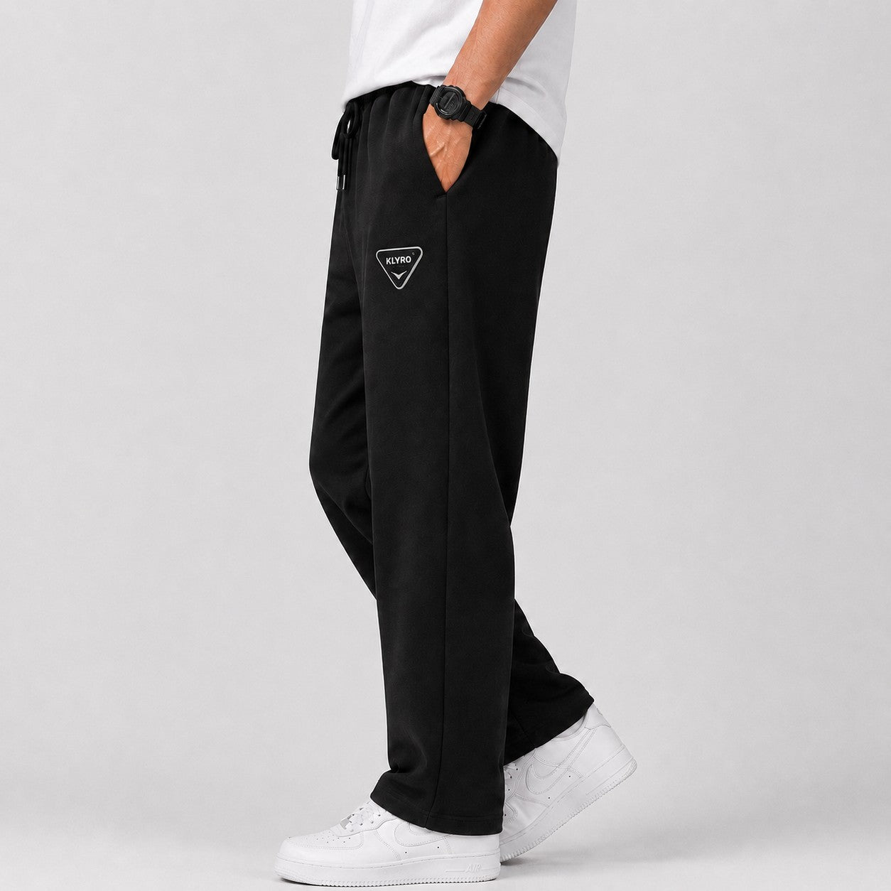KLYRO FASHION men's black athletic track pants with a drawstring waist and logo patch, worn with white sneakers.